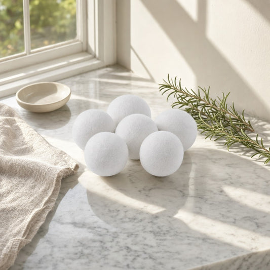 Six white wool dryer balls on a sunlit marble counter