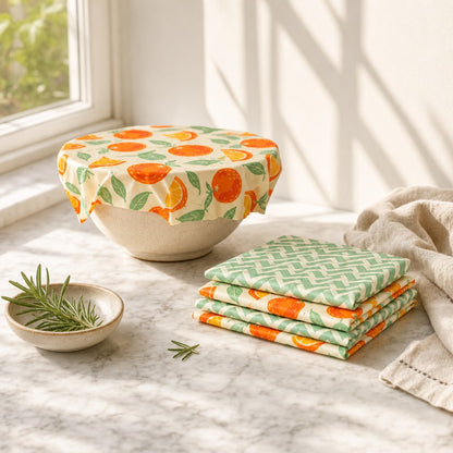 Beeswax food wraps covering a bowl and folded in a stack on a sunlit marble counter